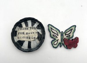 An image of a handmade ceramic bowl which reads "thank you for never giving up". Next to it is a pair of handmade ceramic butterflies.